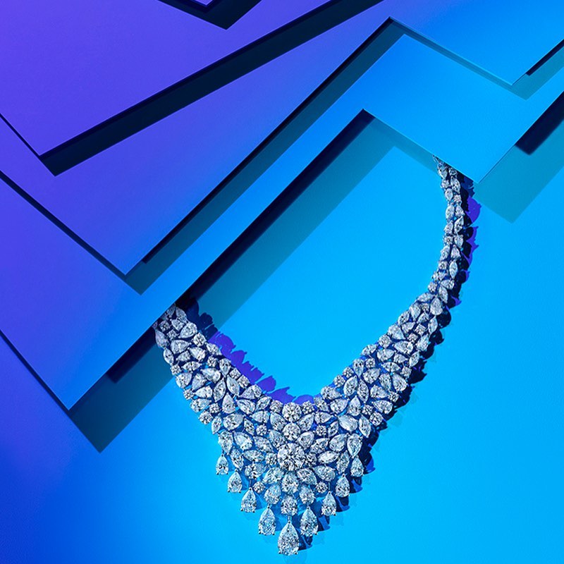 Elegant diamond necklace displayed on a geometric blue background, highlighted by contrasting shades and sharp lines, luxury jewelry.