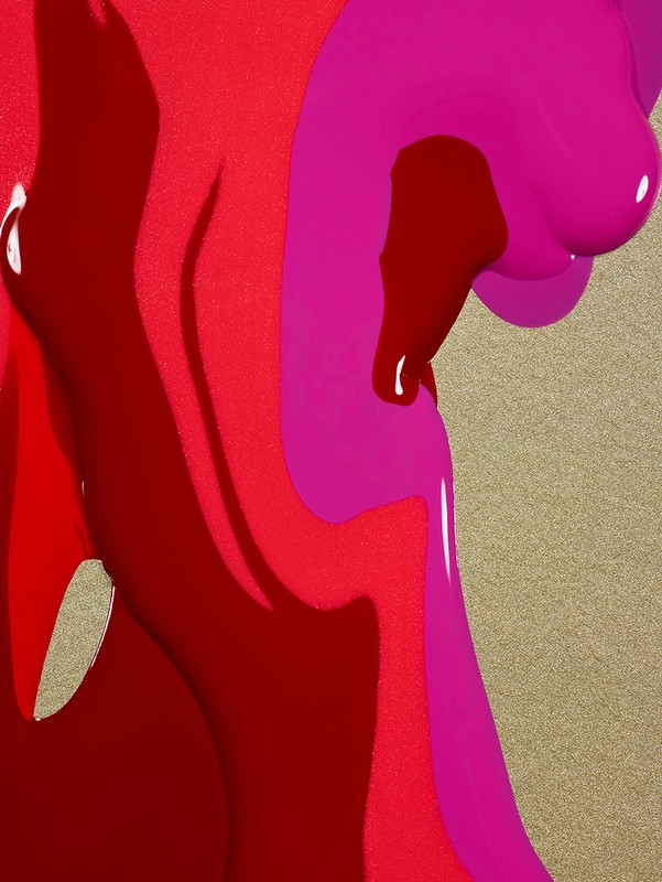 Abstract close-up of dripping red and pink nail polish over a gold surface creating a textured and colorful visual.