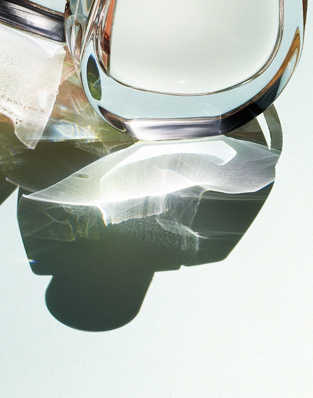 Abstract still life of a clear glass pitcher filled with liquid, accompanied by white cloth under bright studio lighting.