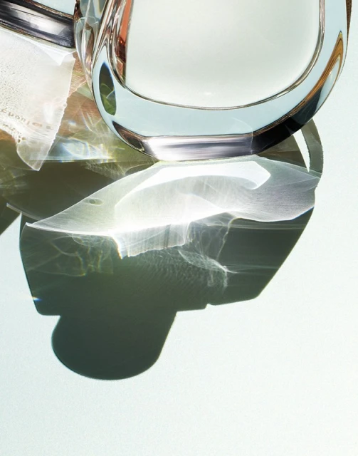 Abstract still life of a clear glass pitcher filled with liquid, accompanied by white cloth under bright studio lighting.