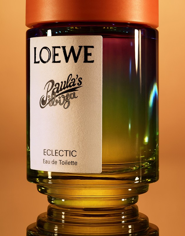 Close-up studio shot of Loewe Paula's Ibiza Eclectic Eau de Toilette glass bottle with orange cap, set on a reflective surface.