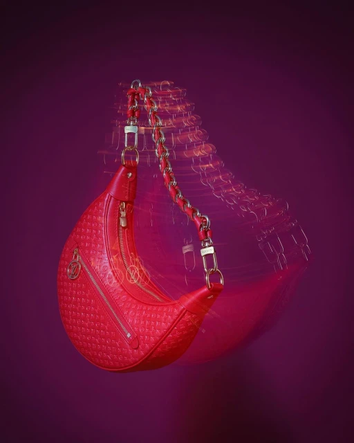 Studio shot of a vibrant red shoulder bag with chain strap against a deep purple backdrop, showcasing high fashion style and design.