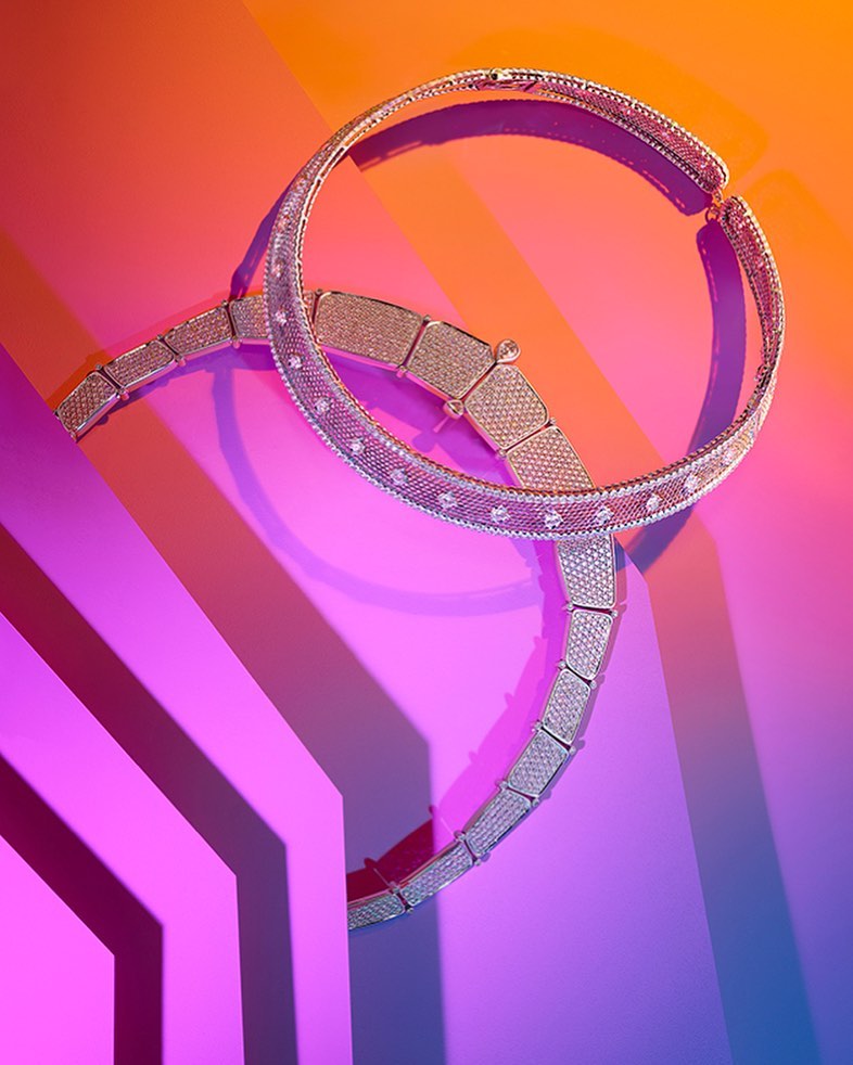 Two diamond-pavé necklaces arranged on a vibrant geometric neon pink, orange, and blue studio background by Coppi Barbieri.