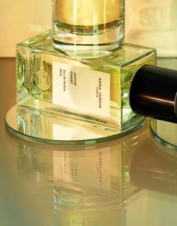 Close-up product photography of perfume bottles resting on a round mirror surface with warm golden lighting and reflections.