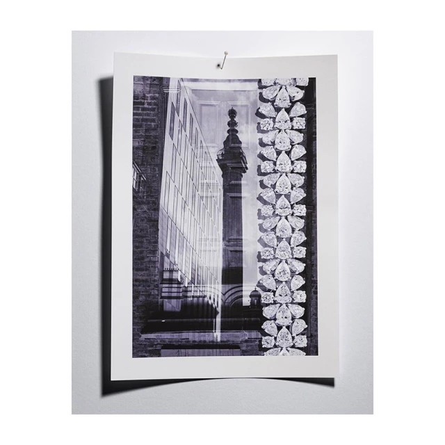 Monochromatic photograph of a print featuring a modern glass building juxtaposed with a classic stone structure and jewelry motifs.