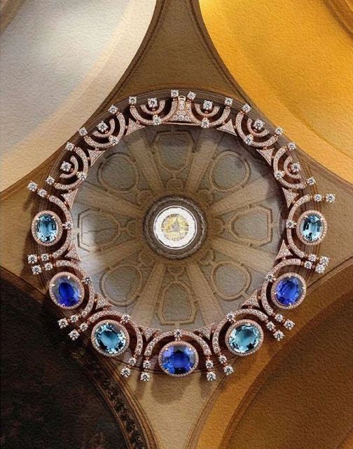 Elegant necklace featuring blue and light blue gemstones and diamonds set against a backdrop of an ornate architectural dome.