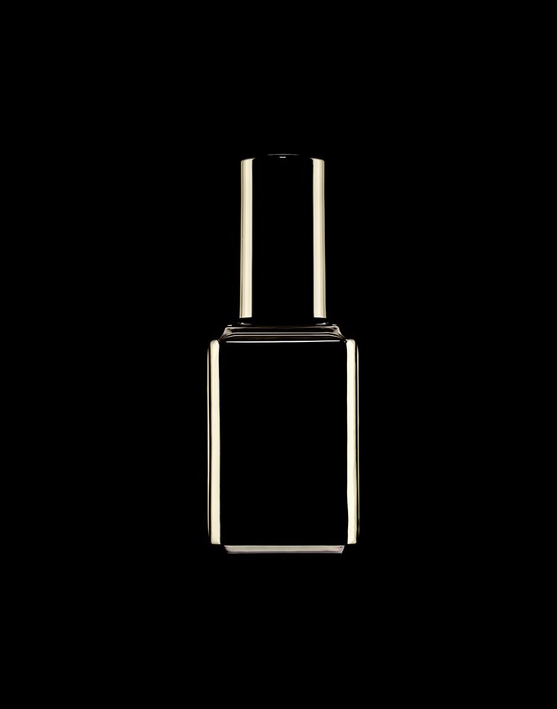 Isolated product shot of a reflective nail polish bottle with a rectangular body and cylinder neck against a solid black backdrop.