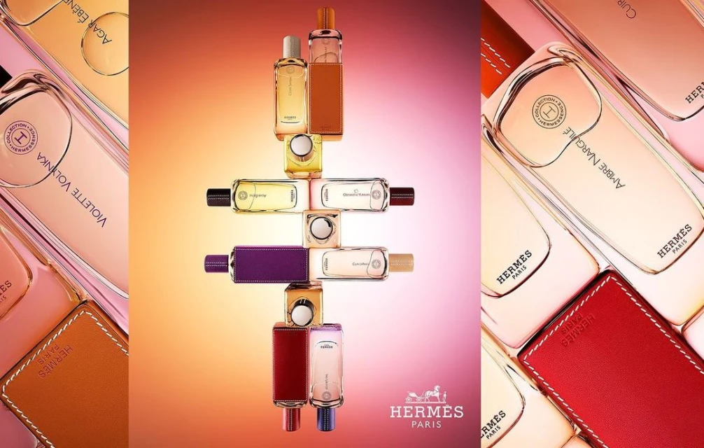 Arrangement of Hermès perfume bottles in various colors and shapes, stacked and aligned against a gradient background. Luxury brand display.
