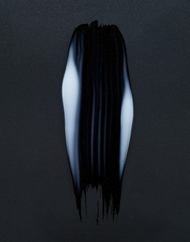 Abstract close-up of a textured brushstroke of black paint with white highlights on a dark background, creating a striking visual contrast.