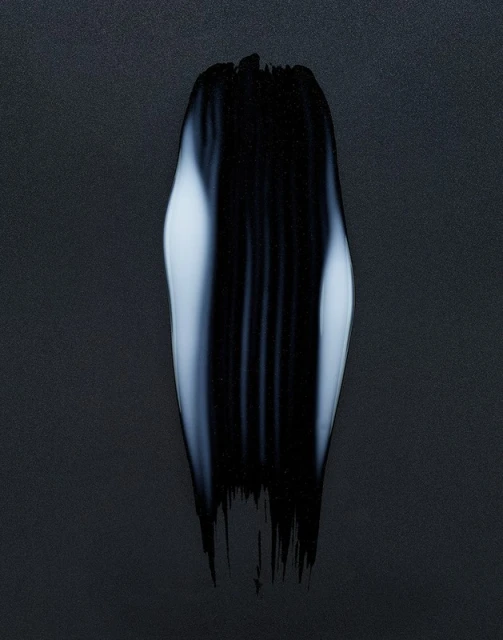 Abstract close-up of a textured brushstroke of black paint with white highlights on a dark background, creating a striking visual contrast.