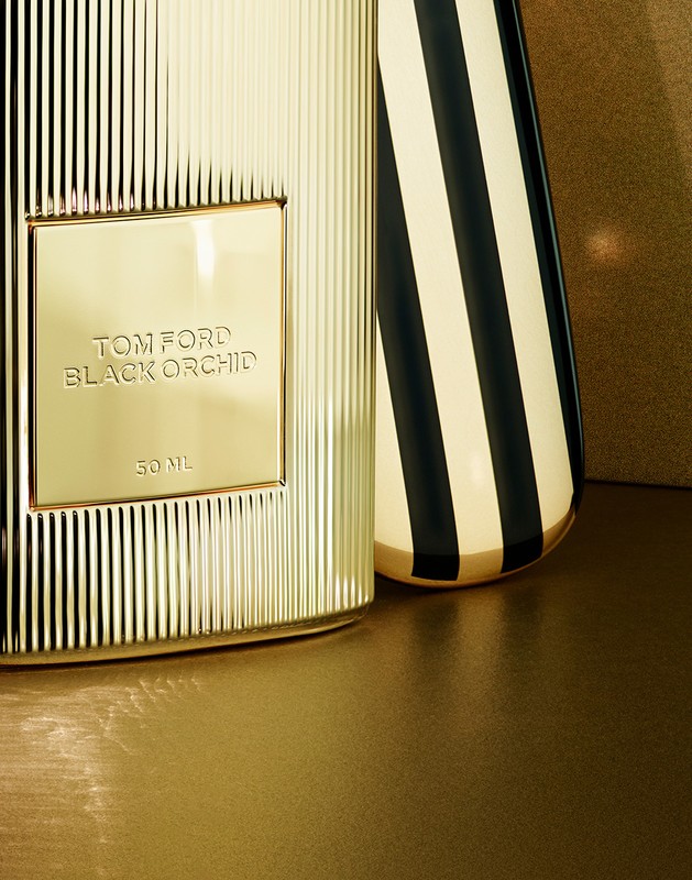 Close-up of a gold Tom Ford Black Orchid perfume bottle with black and gold striped vase against a gold background.