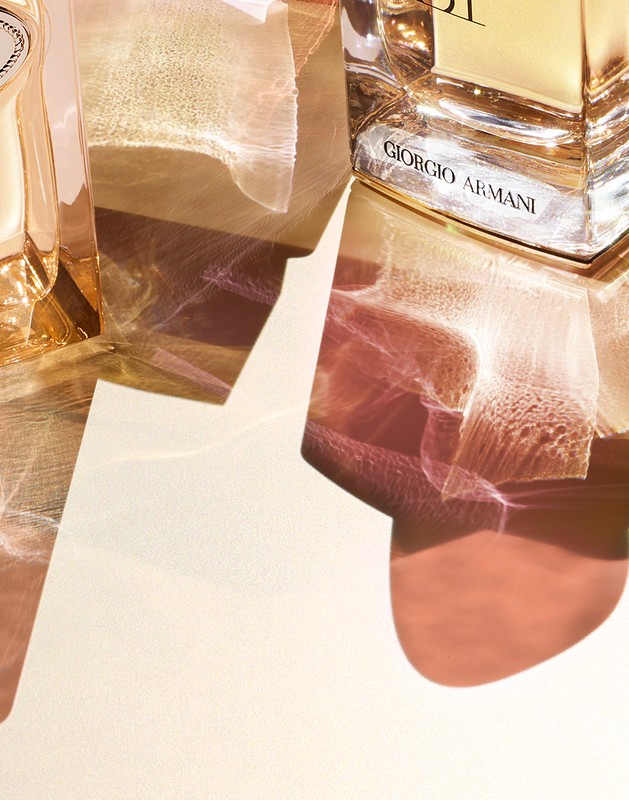 Close-up studio shot of two golden perfume bottles with geometric light patterns on a light peach backdrop for beauty and cosmetics advertising.