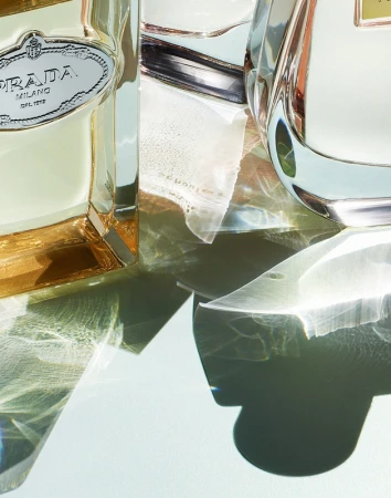 Two perfume bottles, one square and one round, with refracted light patterns against a soft blue background, showcasing minimalist design.