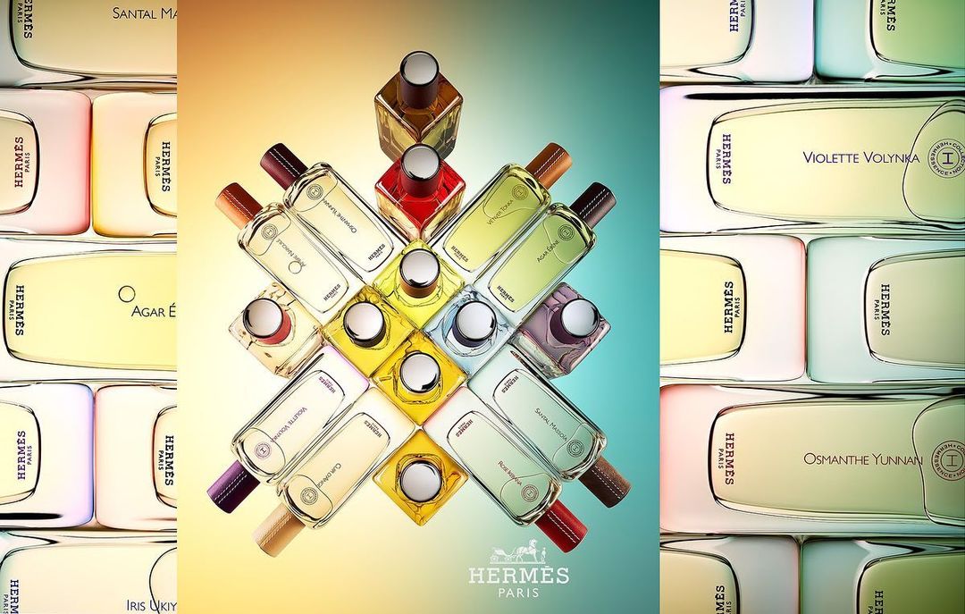 Still life showcasing multiple Hermès perfume bottles with varying color liquid, arranged in a pattern against a gradient background.