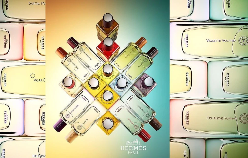 Still life showcasing multiple Hermès perfume bottles with varying color liquid, arranged in a pattern against a gradient background.