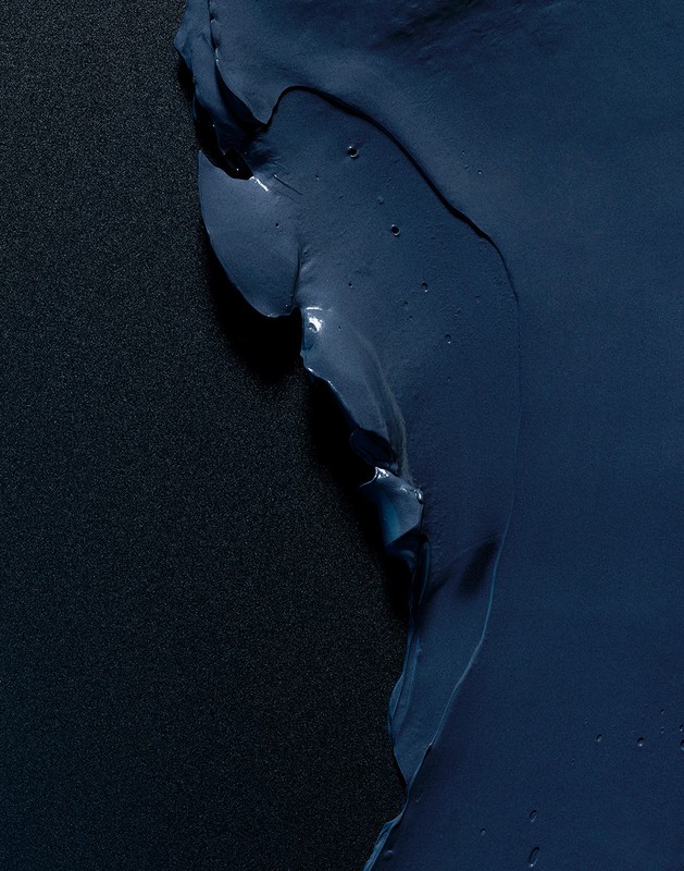 Abstract close-up of dark blue paint smear or thick liquid against a textured black background, creating a modern artistic effect.