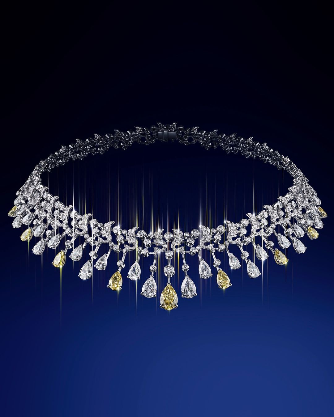 Elegant white gold necklace with yellow and white diamonds arranged in a floral pattern on a deep blue gradient background.