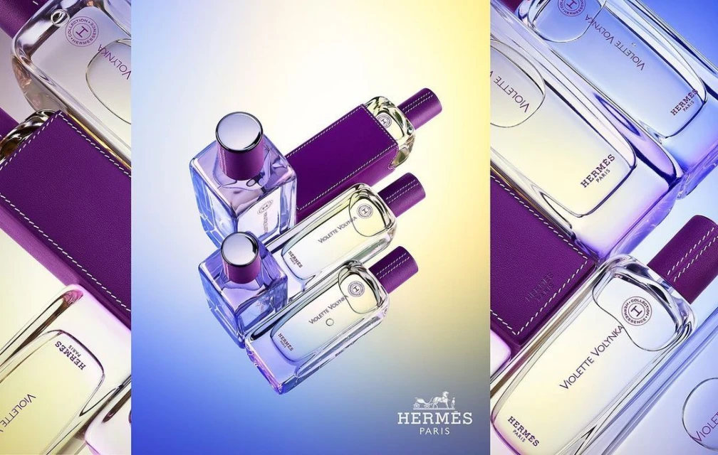 Several HERMÈS Violette Volynka perfume bottles and leather cases are displayed on a light gradient backdrop in a product shot.