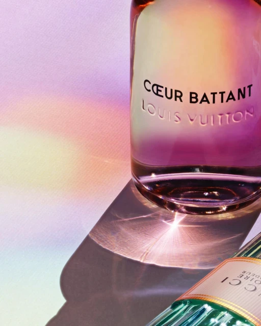 Close-up of Louis Vuitton 'Coeur Battant' and partial Gucci perfume bottles on surface with refracted light; beauty and fashion concept.
