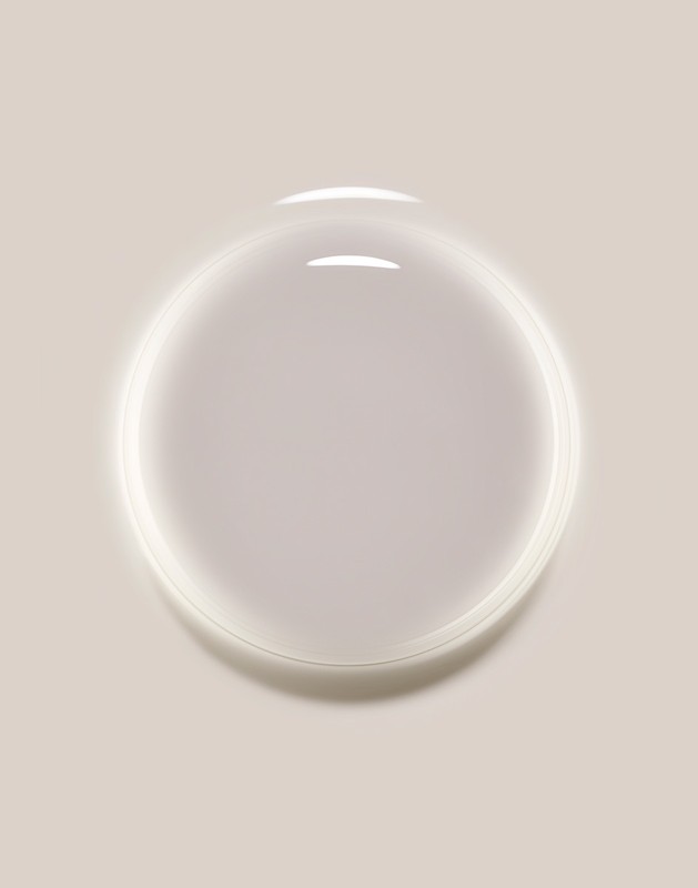 Close-up studio shot of a transparent liquid drop or cosmetic serum, with a clear, glossy texture and subtle light reflections on a tan backdrop.