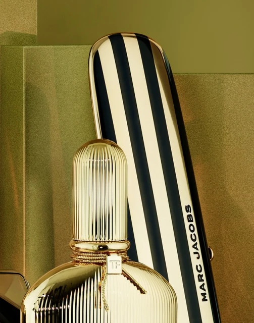 Close-up studio shot of a gold Tom Ford perfume bottle with a striped Marc Jacobs beauty product in the background, showcasing luxury beauty.