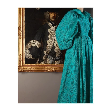 Elegant emerald green gown with a ruffled collar and puff sleeves paired with an ornate gold-framed historical portrait.