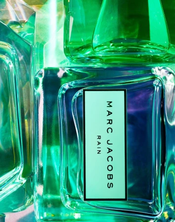 Close-up product photography of Marc Jacobs Rain perfume bottle with emerald green lighting and glass refractions