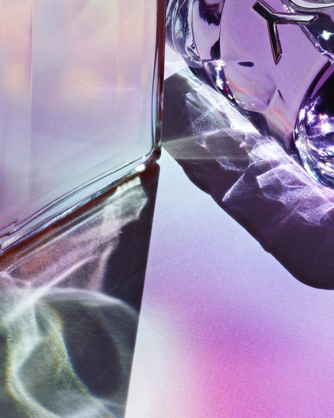 Abstract beauty shot of two glass perfume bottles with light and shadow patterns in pink, lavender, and white tones, creating a textured effect.
