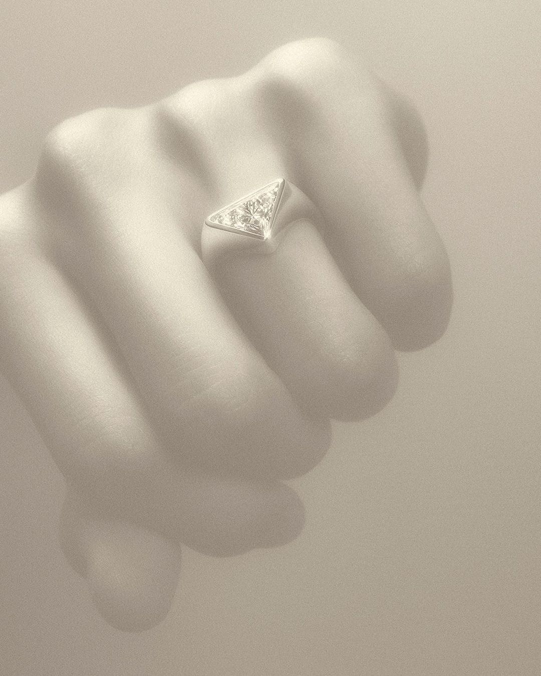 Close-up of a hand wearing a silver, triangular ring with gemstones, set against a neutral background, showcasing jewelry.