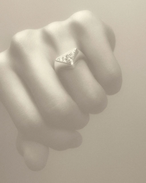 Close-up of a hand wearing a silver, triangular ring with gemstones, set against a neutral background, showcasing jewelry.