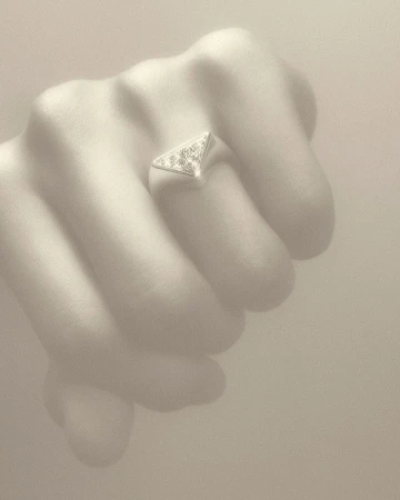 Close-up of a hand wearing a silver, triangular ring with gemstones, set against a neutral background, showcasing jewelry.