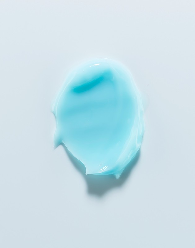 Close-up shot of an aqua-colored cosmetic cream smear on a white background, highlighting its smooth texture and vibrant color.
