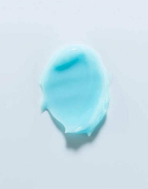 Close-up shot of an aqua-colored cosmetic cream smear on a white background, highlighting its smooth texture and vibrant color.