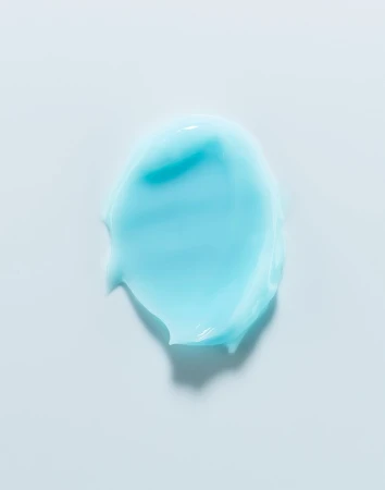 Close-up shot of an aqua-colored cosmetic cream smear on a white background, highlighting its smooth texture and vibrant color.