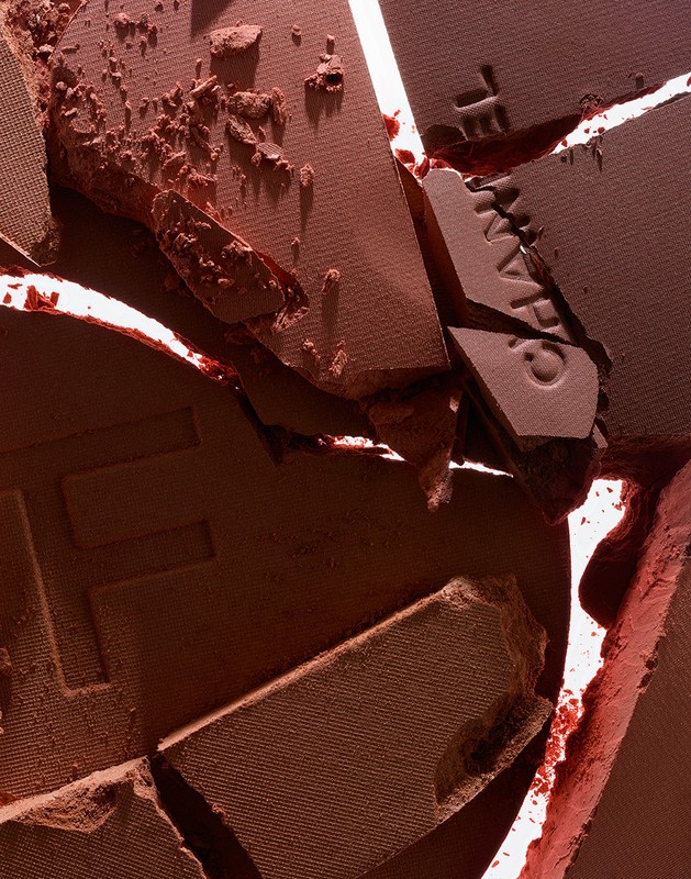 Close-up of cracked and broken terracotta-colored powder makeup. Powder fragments of varying sizes show texture and cosmetic product details.