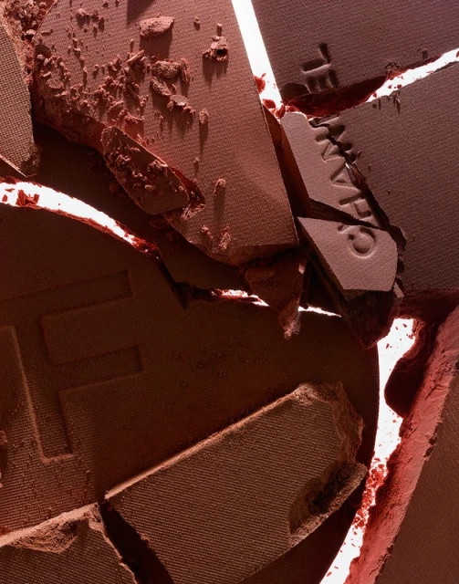 Close-up of cracked and broken terracotta-colored powder makeup. Powder fragments of varying sizes show texture and cosmetic product details.