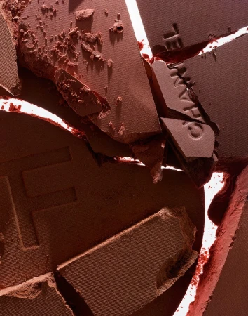 Close-up of cracked and broken terracotta-colored powder makeup. Powder fragments of varying sizes show texture and cosmetic product details.