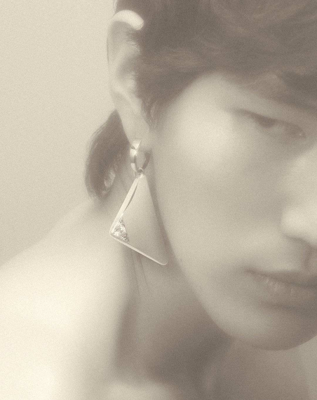 Close-up portrait of a person wearing a large geometric triangular earring, photographed by Coppi Barbieri.