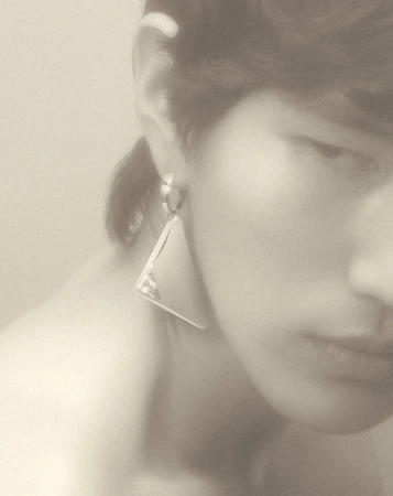 Close-up portrait of a person wearing a large geometric triangular earring, photographed by Coppi Barbieri.