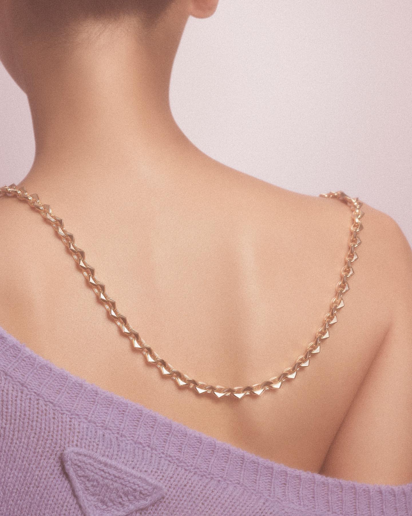 Back view of a woman wearing a gold chain necklace and a lilac sweater, showcasing fashion and beauty.