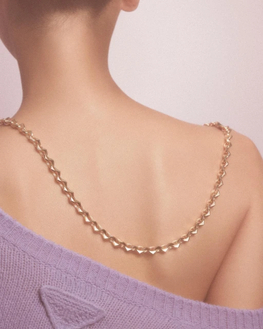 Back view of a woman wearing a gold chain necklace and a lilac sweater, showcasing fashion and beauty.