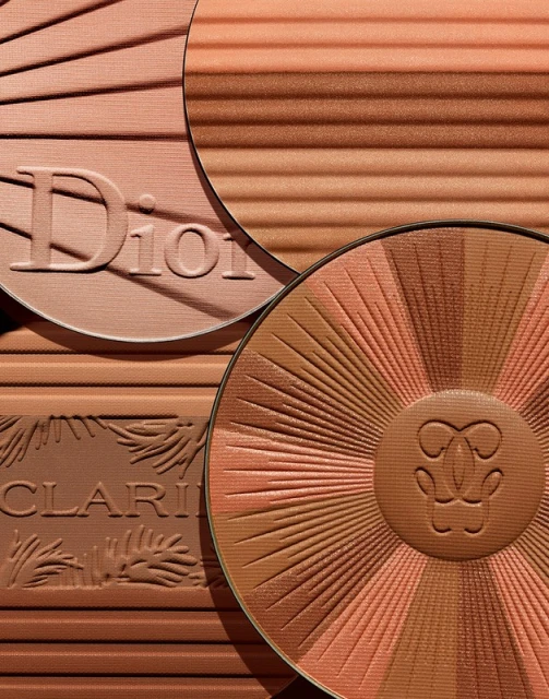 Close-up studio shot of bronzer palettes by Dior, Guerlain, and Clarins, featuring warm, earthy tones, and radiating sunburst patterns.