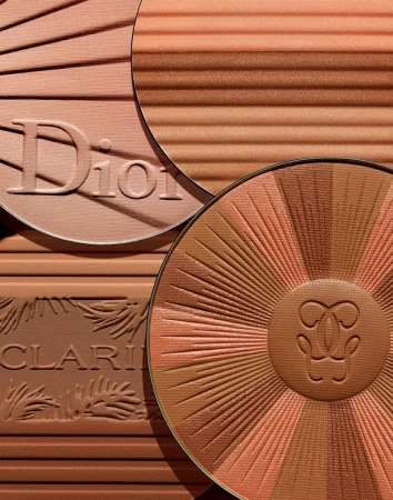 Close-up studio shot of bronzer palettes by Dior, Guerlain, and Clarins, featuring warm, earthy tones, and radiating sunburst patterns.