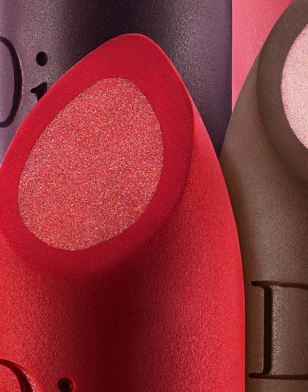 Close-up studio shot of red, brown, and purple makeup sponges with a textured finish, illuminated by soft lighting and cropped composition.