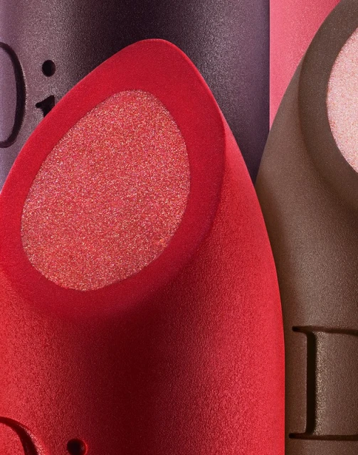 Close-up studio shot of red, brown, and purple makeup sponges with a textured finish, illuminated by soft lighting and cropped composition.