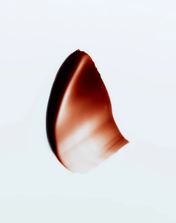 Close-up studio shot of a smear of dark brown cosmetic product, set against a clean white backdrop. Rich textures and color contrast.
