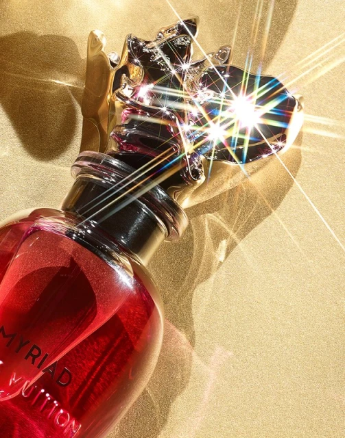 Close-up studio shot of a red Myriad Louis Vuitton perfume bottle with a decorative gold cap, set against a textured gold background.
