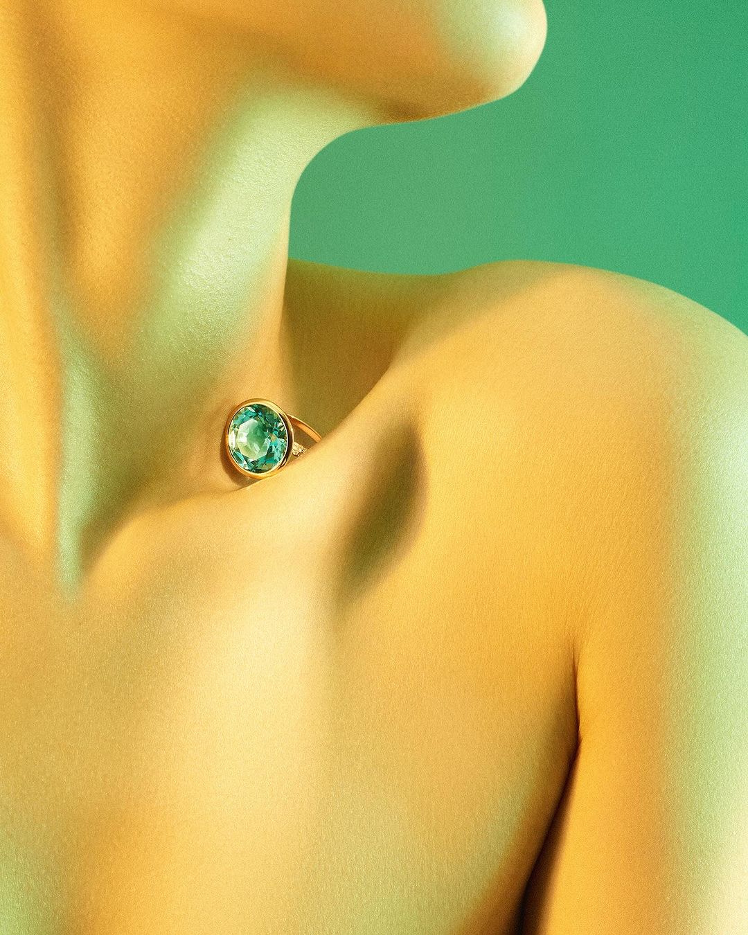 Close-up portrait of a model wearing a gold ring with a large blue gemstone positioned at the hollow of her throat by Coppi Barbieri
