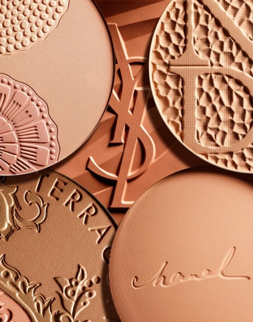 Macro shot of luxury cosmetic compacts featuring embossed brand logos and intricate designs, showcasing high-end beauty and texture.