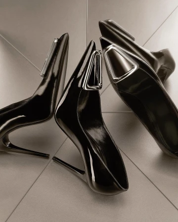 Studio shot of three black patent leather high heel shoes with silver hardware accents on a glossy tile surface, fashion forward footwear.